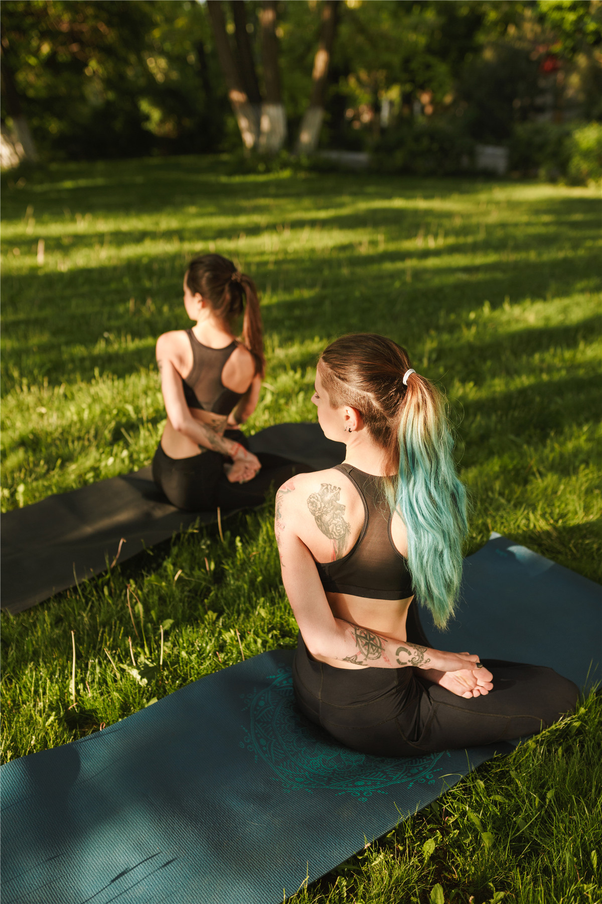 dua wanita-muda-hitam-atasan-sporty-legging-duduk-dari-punggung-melatih-yoga-berpose-bersama-wanita-muda-berlatih-yoga-di luar ruangan